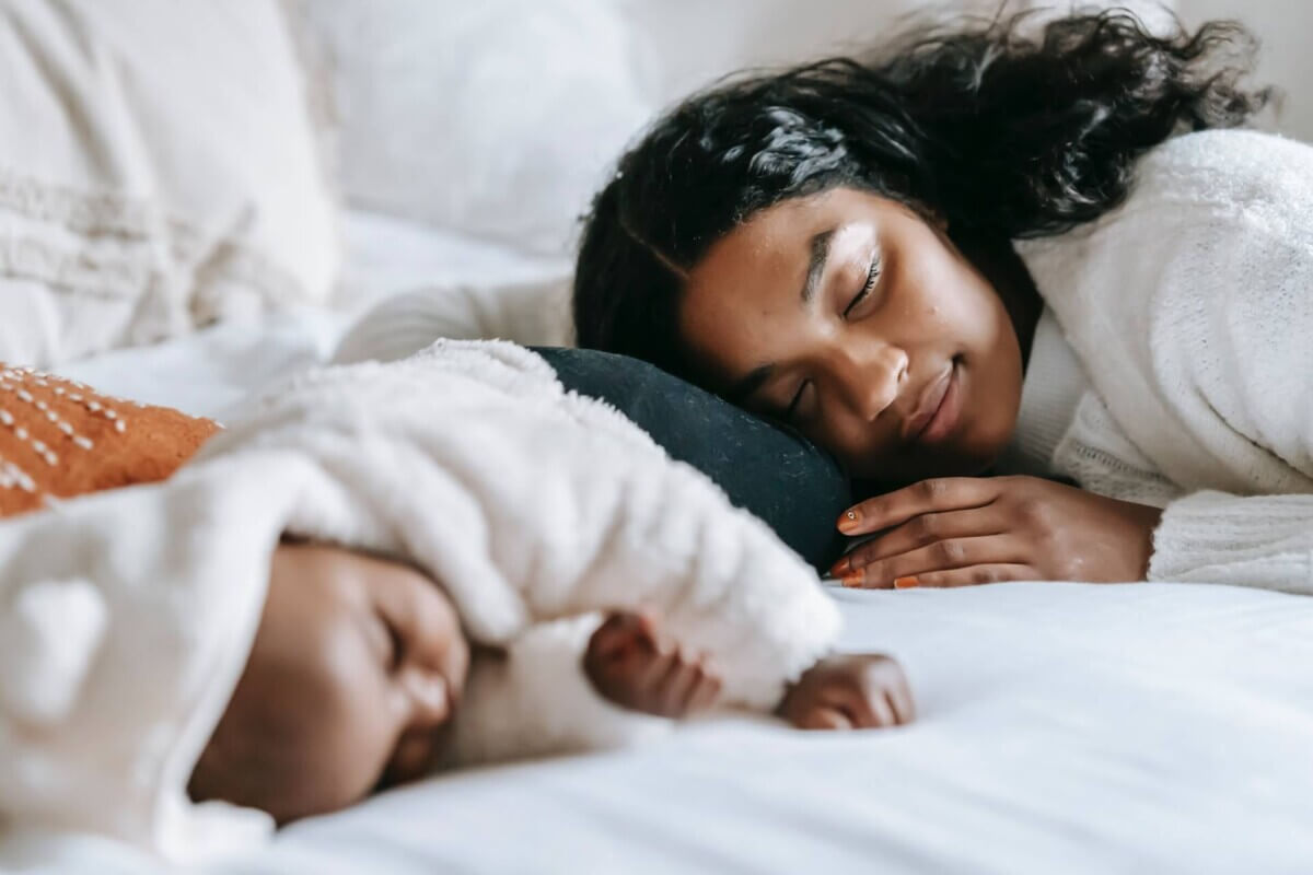 A mother and her sleeping baby resting peacefully together on a bed.